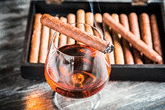 Burning cigar on glass with cognac on old wooden table