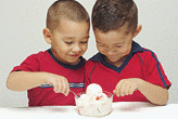 Two preschool brothers dig into a large bowl of strawberry-cheesecake ice cream