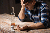 unhappy drunk man with bottle of alcohol and pills committing suicide by overdosing on medication at night