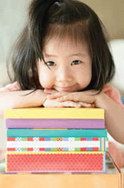 Asian toddler puts her chin on stack of books