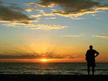 An elderly man watches a beautiful sunset at the sea.