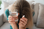 Upset young woman with abortion pill and glass of water at home