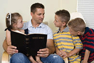 A father reads to his three young children from the Holy Bible.