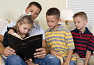 A father reads to his three young children from the Holy Bible.