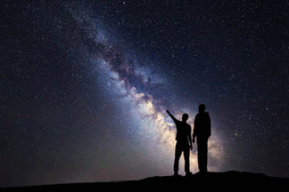 A silhouette of a father and a son who is pointing a finger in the night starry sky in the background of Milky Way.