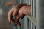 Man's hands through a jail cell door.