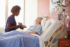 A hospital nurse with a tablet talks to a senior patient.