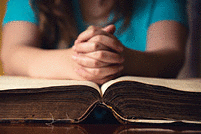 Someone praying with their hands on a Bible