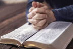 A person is praying with hands on his Bible.